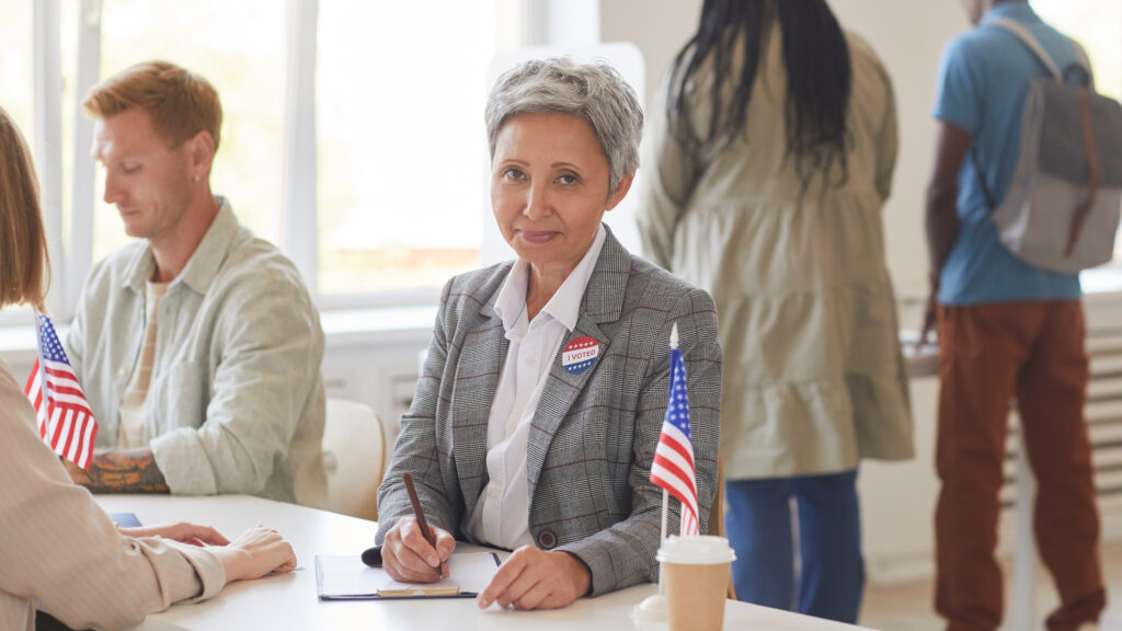 Portrait of modern mature woman registering voters while working at desk on election day